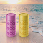 Load image into Gallery viewer, Two NOZ yellow and purple nose stick sunscreen in front to the beach.
